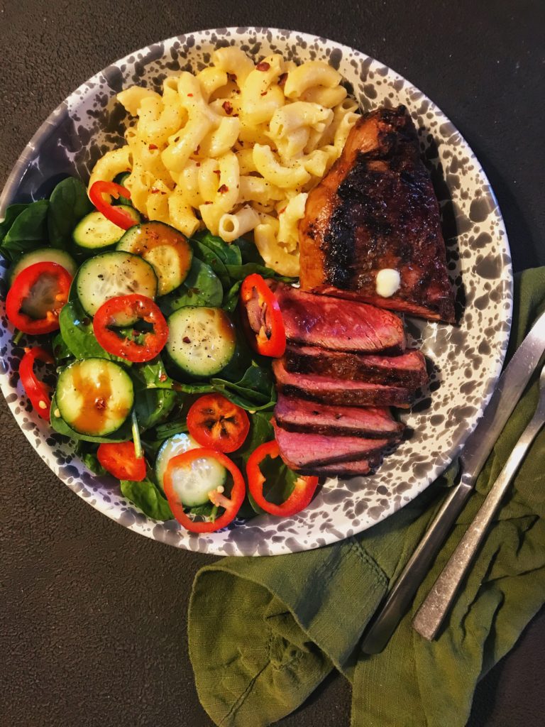 Mac and cheese on a plate with steak and salad.