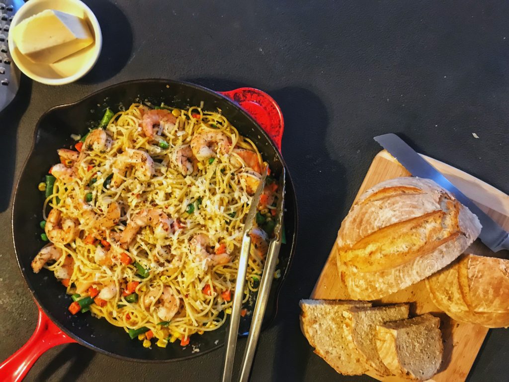 shrimp scampi in a skillet with a loaf of fresh bread alongside