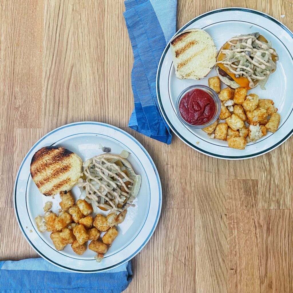 Whiskey mushroom burgers on plates with tater tots and blue napkins